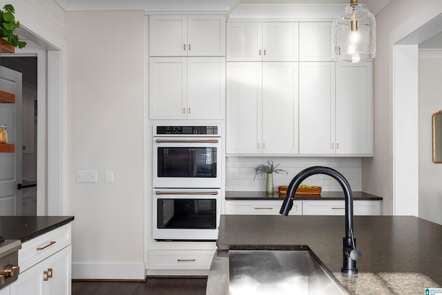 kitchen with tasteful backsplash, double oven, sink, white cabinets, and hanging light fixtures