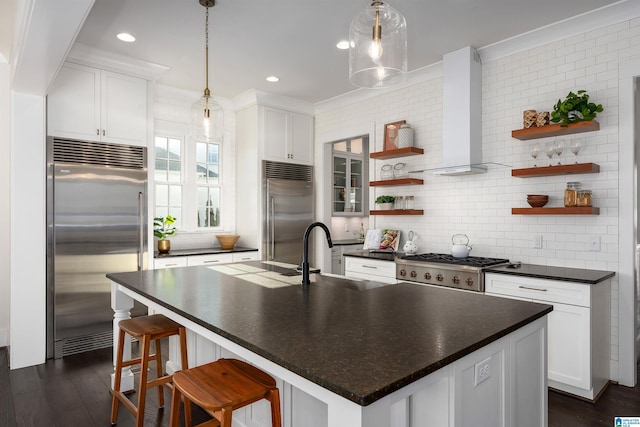 kitchen featuring a center island with sink, wall chimney exhaust hood, decorative backsplash, and appliances with stainless steel finishes