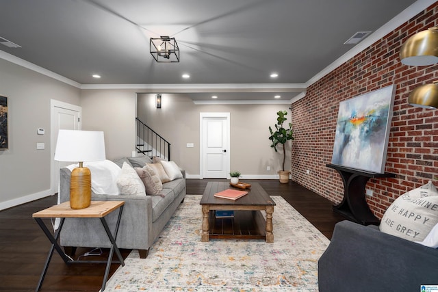 living room featuring dark hardwood / wood-style flooring, an inviting chandelier, crown molding, and brick wall