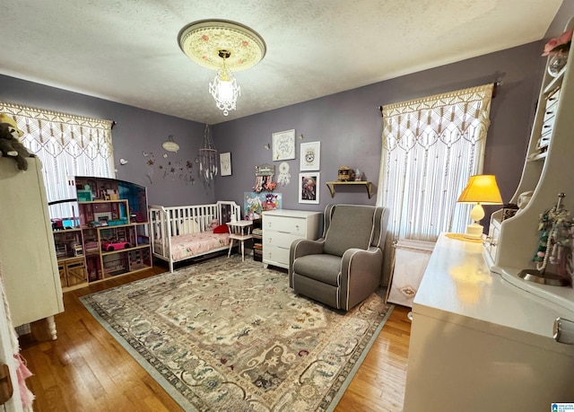 bedroom featuring a crib, a textured ceiling, and hardwood / wood-style flooring