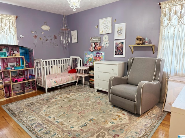 bedroom with hardwood / wood-style flooring, a nursery area, a textured ceiling, and a chandelier