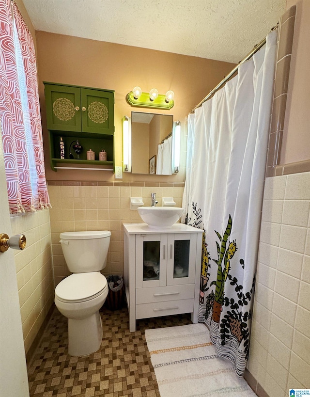 bathroom featuring vanity, a textured ceiling, toilet, and tile walls