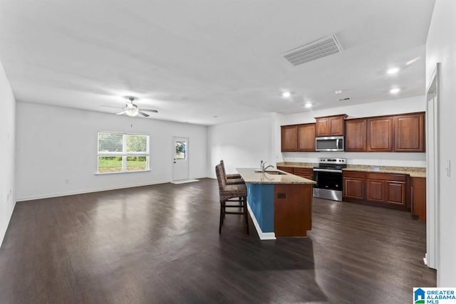 kitchen featuring a center island with sink, ceiling fan, appliances with stainless steel finishes, a kitchen breakfast bar, and sink