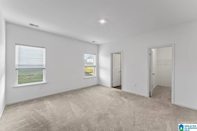 unfurnished bedroom featuring a spacious closet, a closet, and light carpet