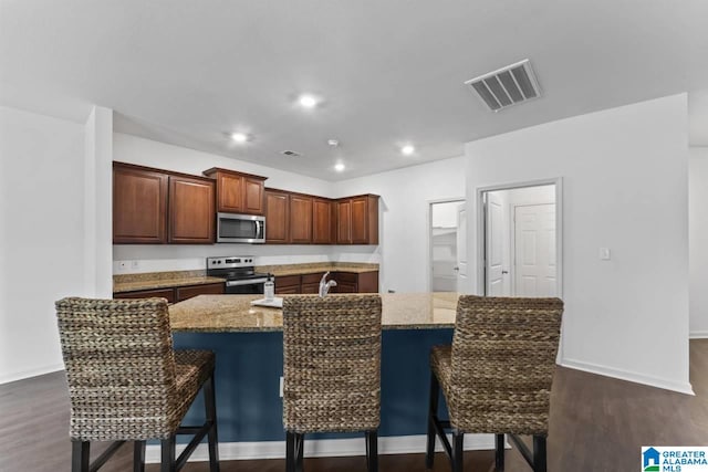 kitchen featuring light stone countertops, appliances with stainless steel finishes, a kitchen island with sink, and a breakfast bar area