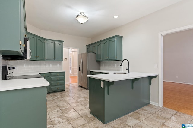 kitchen with kitchen peninsula, stainless steel fridge with ice dispenser, green cabinets, and range