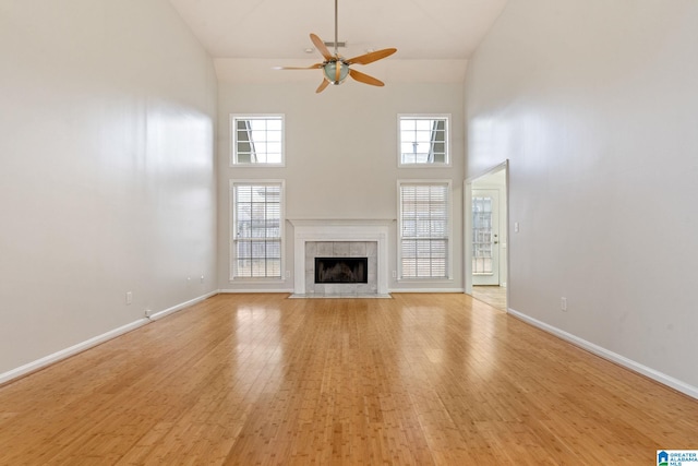 unfurnished living room with ceiling fan, a fireplace, a high ceiling, and light wood-type flooring