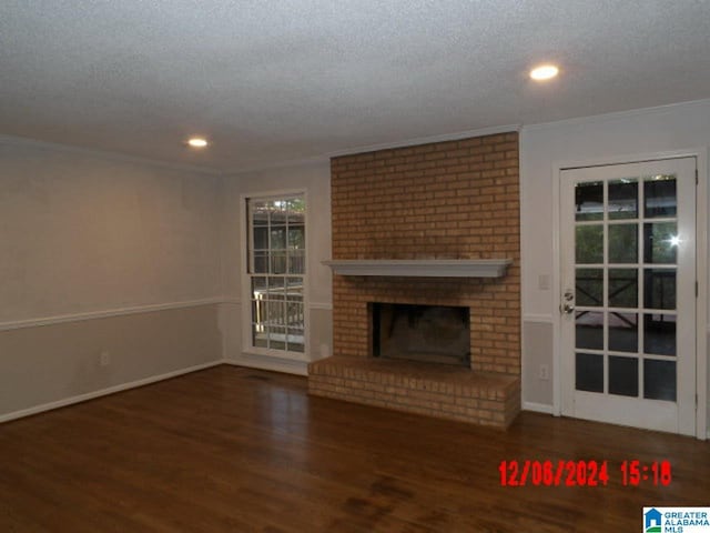 unfurnished living room featuring ornamental molding, dark hardwood / wood-style floors, a textured ceiling, and a brick fireplace