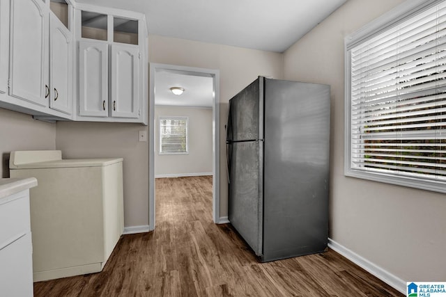 kitchen featuring black refrigerator, white cabinets, washer / clothes dryer, and hardwood / wood-style flooring