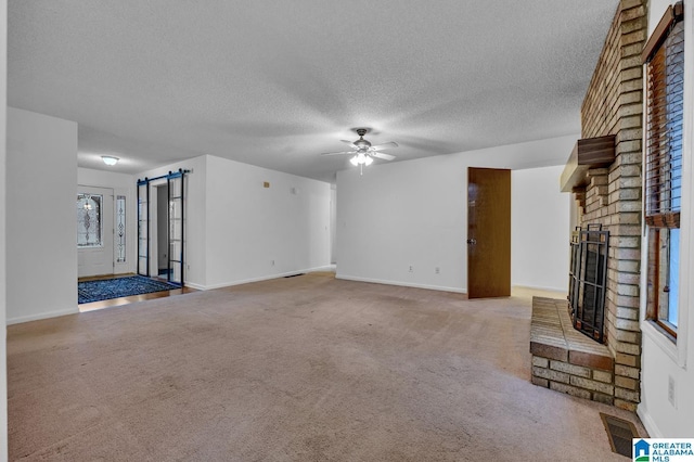 unfurnished living room with ceiling fan, light colored carpet, a textured ceiling, and a brick fireplace