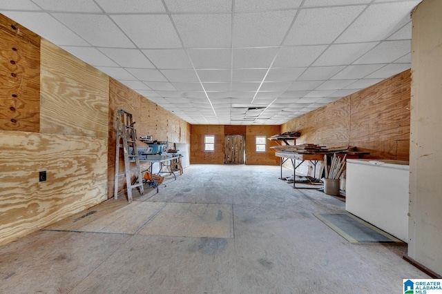 basement featuring a drop ceiling and wood walls