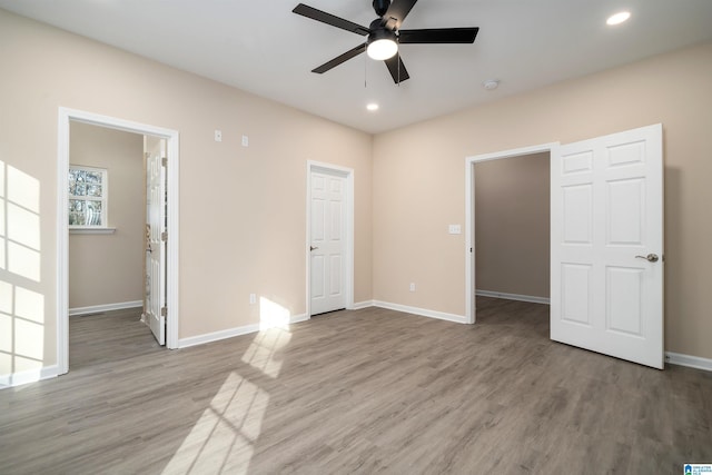 unfurnished bedroom featuring ceiling fan, a walk in closet, connected bathroom, and hardwood / wood-style floors