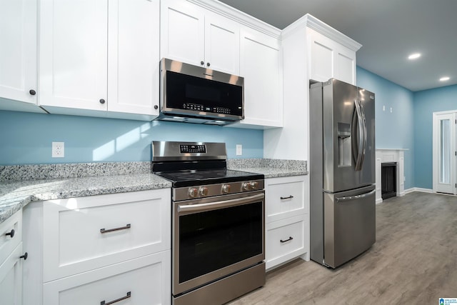 kitchen with light hardwood / wood-style floors, light stone countertops, white cabinets, and stainless steel appliances