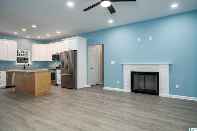 kitchen with ceiling fan, appliances with stainless steel finishes, light wood-type flooring, white cabinets, and a center island