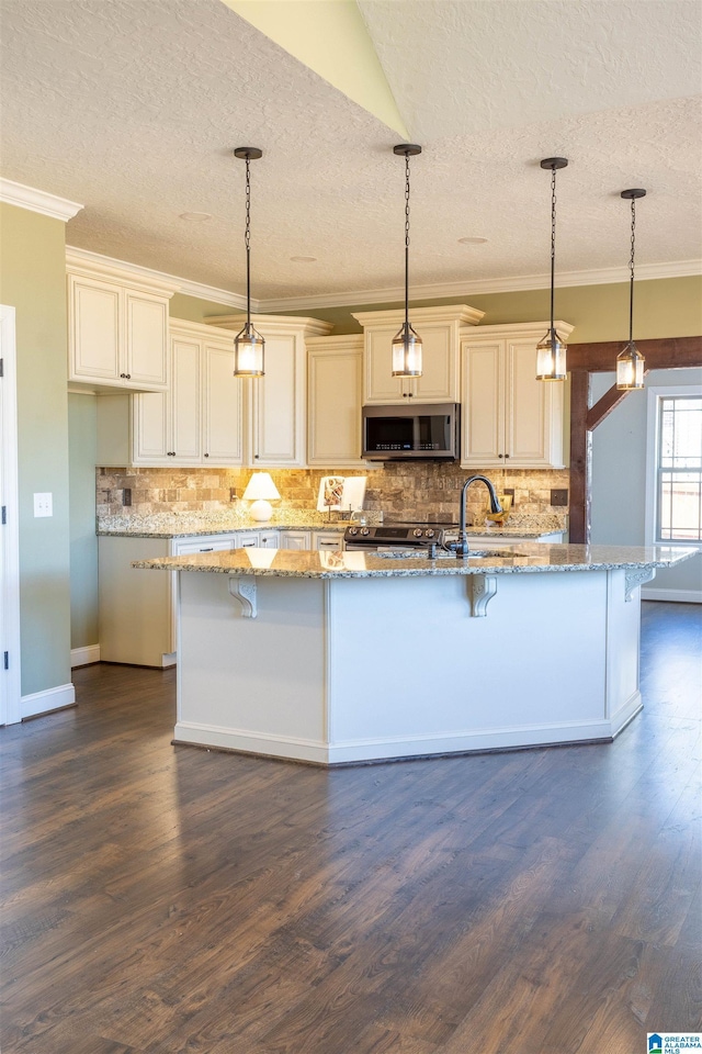 kitchen with cream cabinetry, light stone countertops, hanging light fixtures, and a breakfast bar area