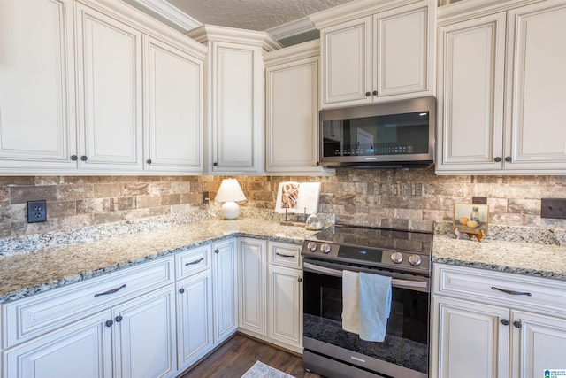 kitchen with cream cabinets, decorative backsplash, light stone countertops, ornamental molding, and appliances with stainless steel finishes