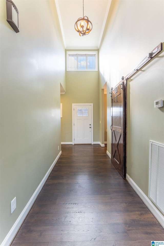 doorway featuring crown molding, a towering ceiling, dark hardwood / wood-style floors, and an inviting chandelier