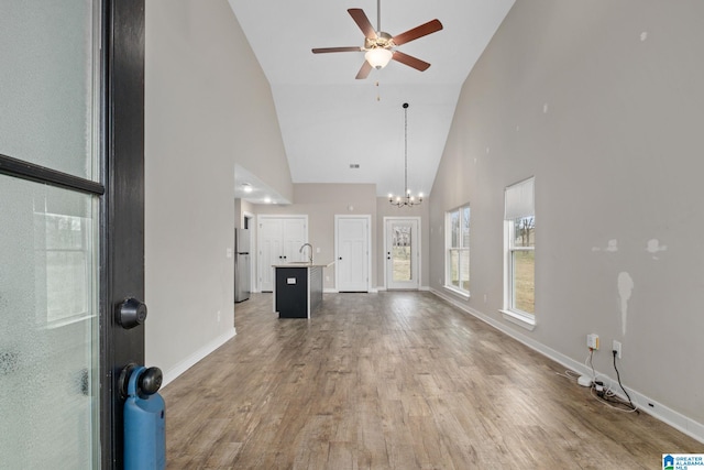 unfurnished living room featuring hardwood / wood-style flooring, ceiling fan with notable chandelier, sink, and high vaulted ceiling