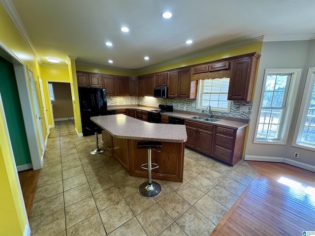 kitchen with a center island, black appliances, sink, ornamental molding, and a breakfast bar area