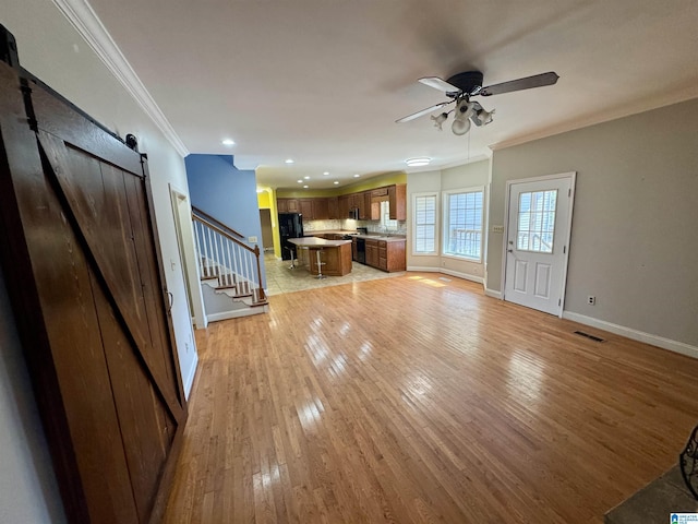 unfurnished living room featuring ceiling fan, a barn door, crown molding, and light hardwood / wood-style flooring