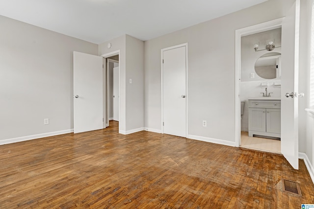 unfurnished bedroom featuring connected bathroom, hardwood / wood-style flooring, and sink