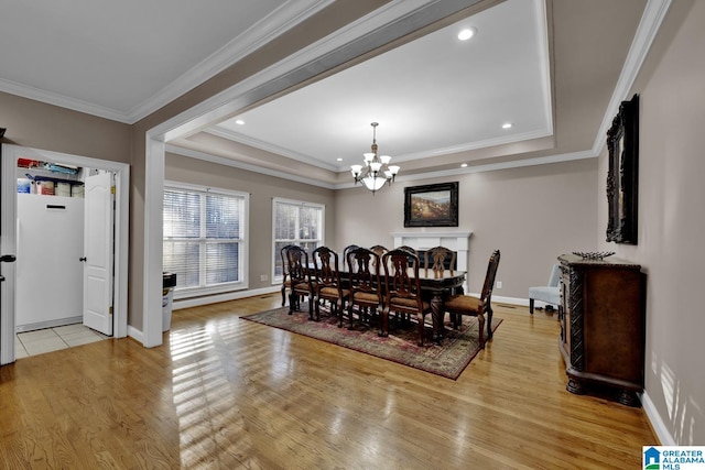 dining room featuring light wood-type flooring, a tray ceiling, an inviting chandelier, and ornamental molding