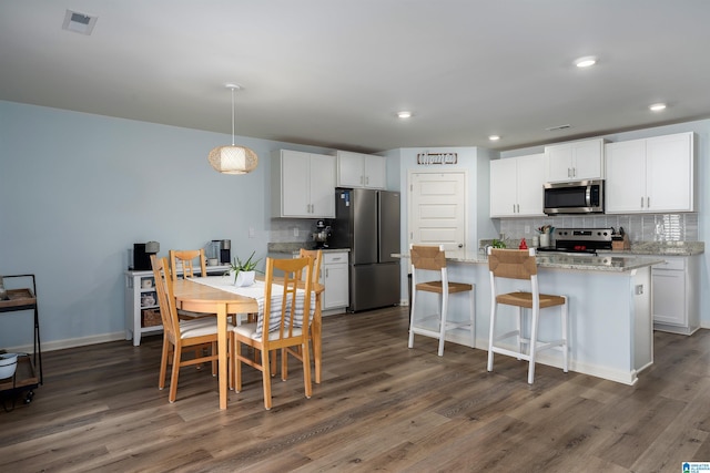 kitchen with appliances with stainless steel finishes, hanging light fixtures, white cabinetry, and decorative backsplash