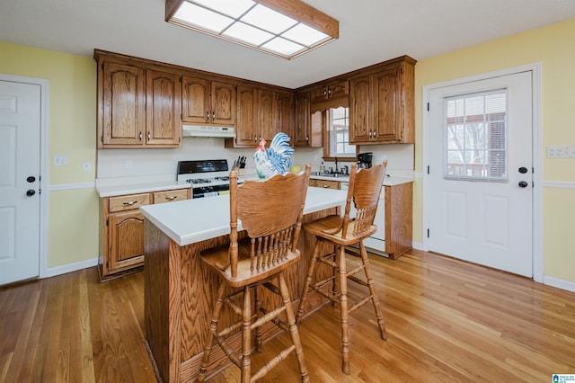 kitchen featuring white range, sink, light hardwood / wood-style floors, a kitchen island, and a breakfast bar area