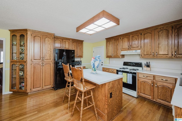 kitchen featuring a center island, black refrigerator with ice dispenser, a kitchen breakfast bar, white gas range oven, and light hardwood / wood-style flooring