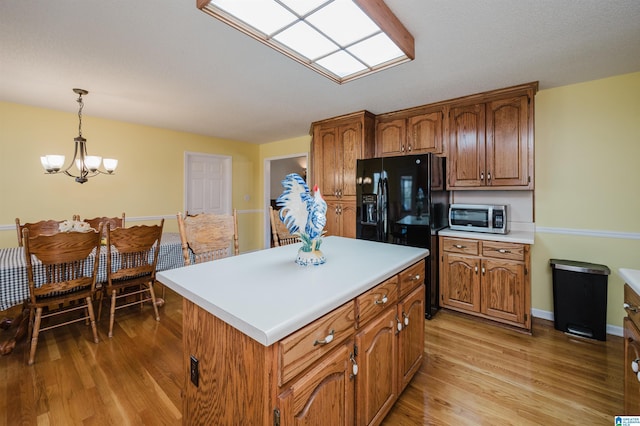 kitchen featuring a center island, hanging light fixtures, a notable chandelier, light hardwood / wood-style floors, and black fridge with ice dispenser