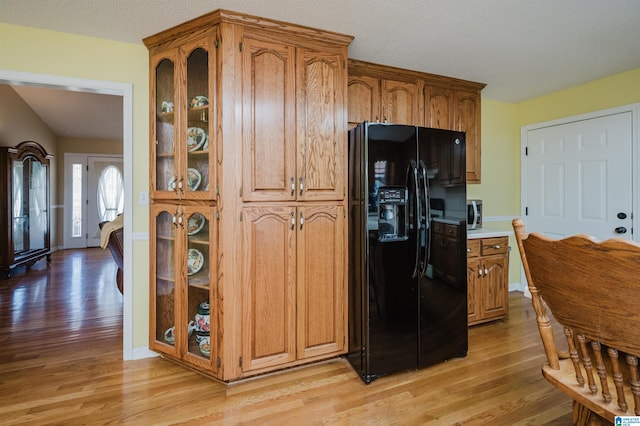 kitchen with a textured ceiling, light hardwood / wood-style flooring, and black refrigerator with ice dispenser