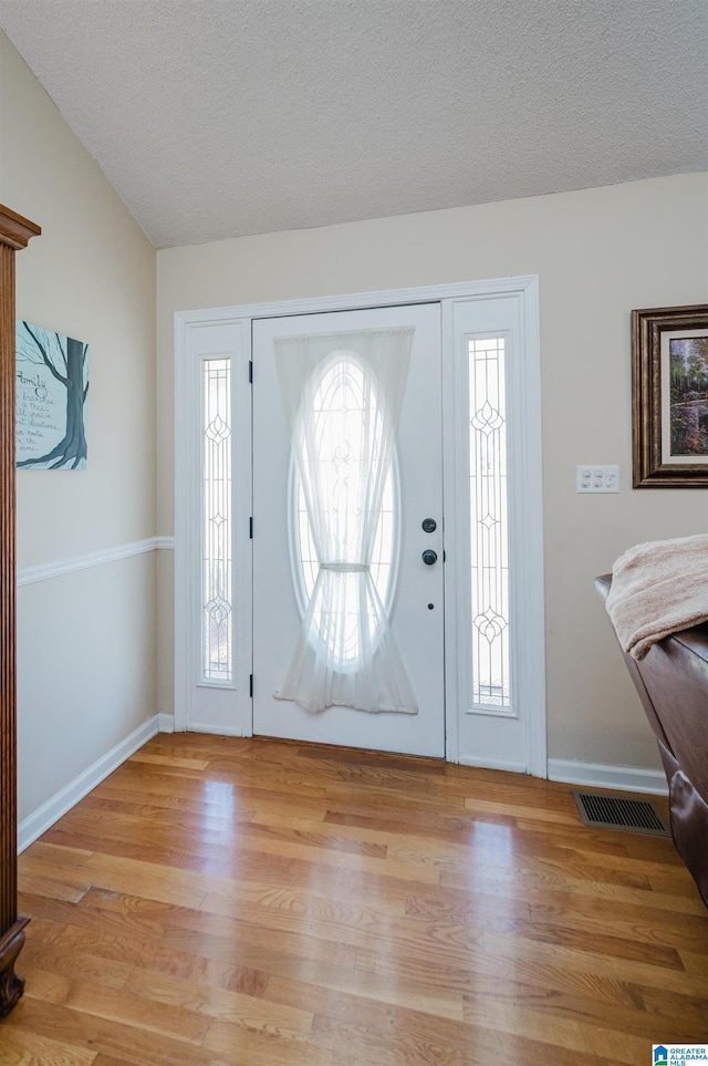 foyer entrance with light hardwood / wood-style floors, lofted ceiling, and a textured ceiling