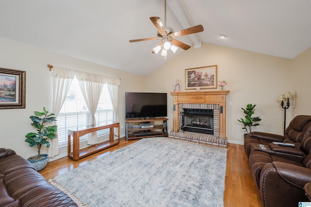 living room featuring vaulted ceiling with beams, ceiling fan, light hardwood / wood-style floors, and a brick fireplace