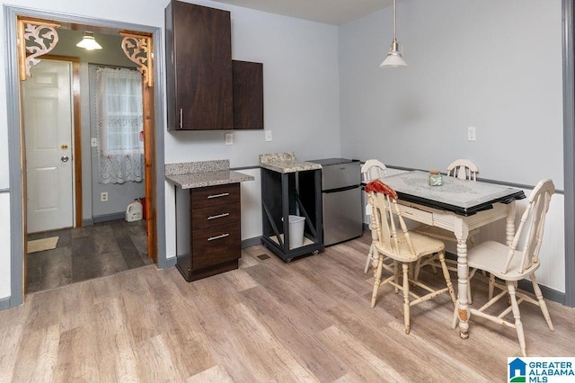 kitchen with stainless steel fridge, dark brown cabinets, decorative light fixtures, and light wood-type flooring