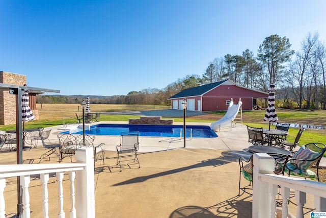 view of swimming pool with a lawn, a water slide, an outbuilding, a water view, and a patio