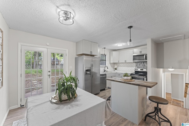 kitchen featuring pendant lighting, sink, decorative backsplash, white cabinetry, and stainless steel appliances