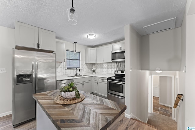 kitchen featuring white cabinets, sink, appliances with stainless steel finishes, tasteful backsplash, and decorative light fixtures