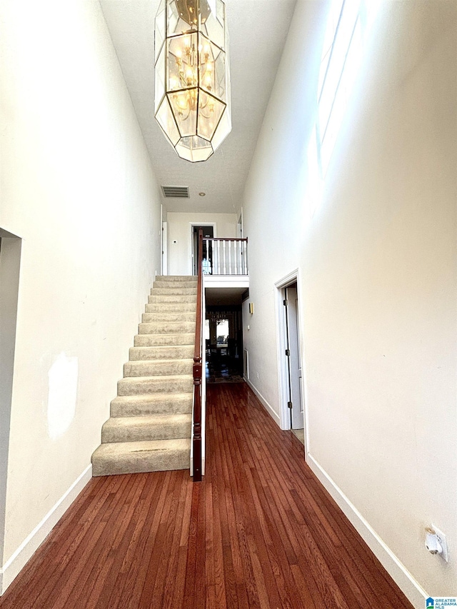 stairs with a towering ceiling, hardwood / wood-style flooring, and a notable chandelier