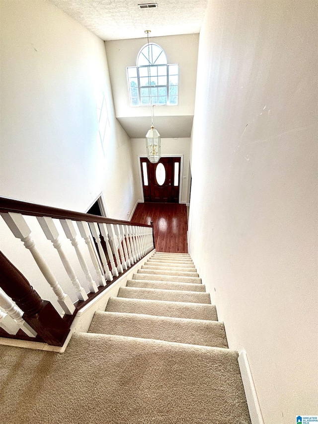 staircase featuring a high ceiling, a textured ceiling, and a notable chandelier