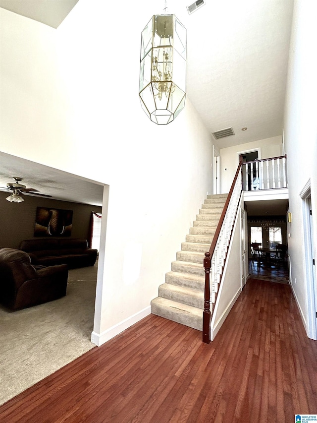 stairs with hardwood / wood-style flooring, ceiling fan with notable chandelier, and a high ceiling