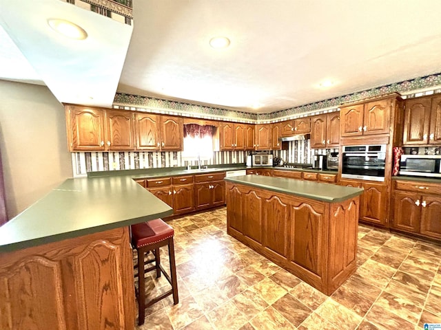 kitchen featuring sink, appliances with stainless steel finishes, a kitchen island, kitchen peninsula, and a breakfast bar area