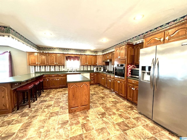 kitchen with sink, kitchen peninsula, a breakfast bar area, a kitchen island, and appliances with stainless steel finishes