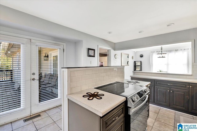 kitchen featuring electric range, decorative backsplash, dark brown cabinets, and light tile patterned floors