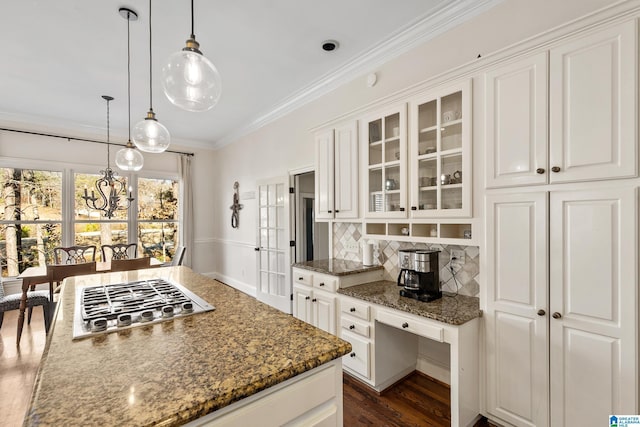 kitchen featuring stainless steel gas stovetop, backsplash, dark stone counters, white cabinets, and decorative light fixtures