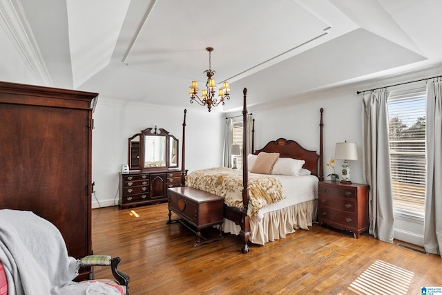 bedroom featuring a tray ceiling, light wood-type flooring, and an inviting chandelier