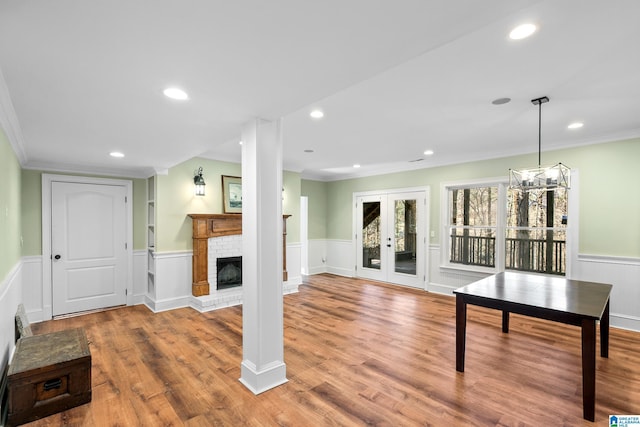 living room with french doors, a brick fireplace, crown molding, hardwood / wood-style floors, and a chandelier