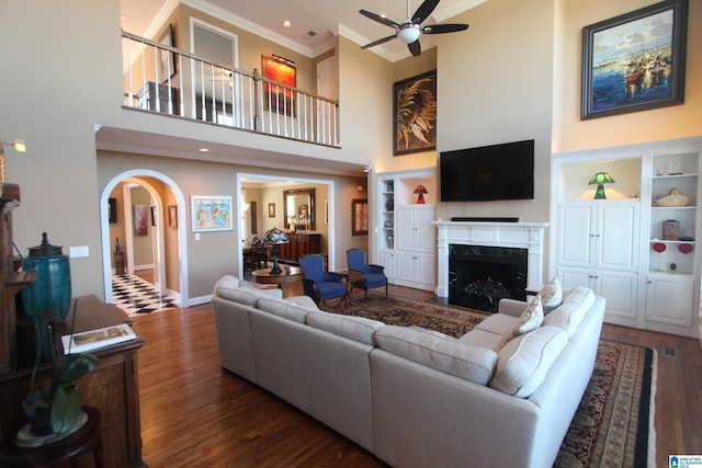 living room with built in shelves, crown molding, dark hardwood / wood-style flooring, and ceiling fan