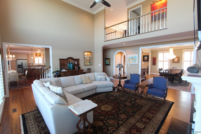 living room featuring crown molding, hardwood / wood-style floors, ceiling fan with notable chandelier, and a high ceiling