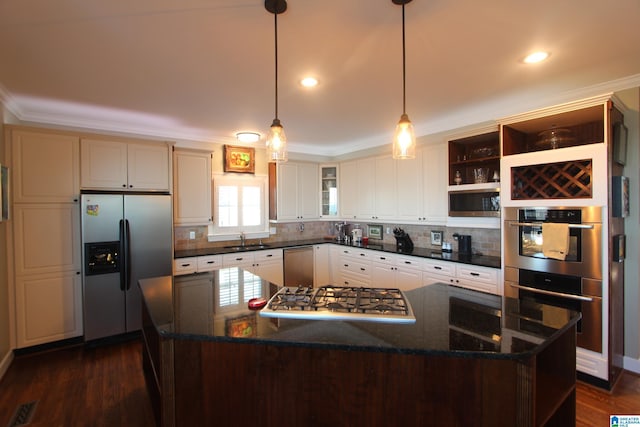 kitchen featuring appliances with stainless steel finishes, dark stone counters, sink, a kitchen island, and hanging light fixtures