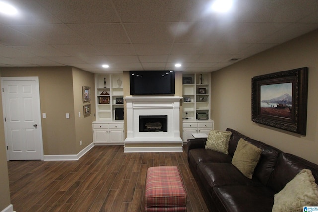 living room with built in shelves, a drop ceiling, and dark hardwood / wood-style floors